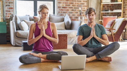 Frau und Mann sitzen auf dem Boden und machen Yogaübungen über Laptop
